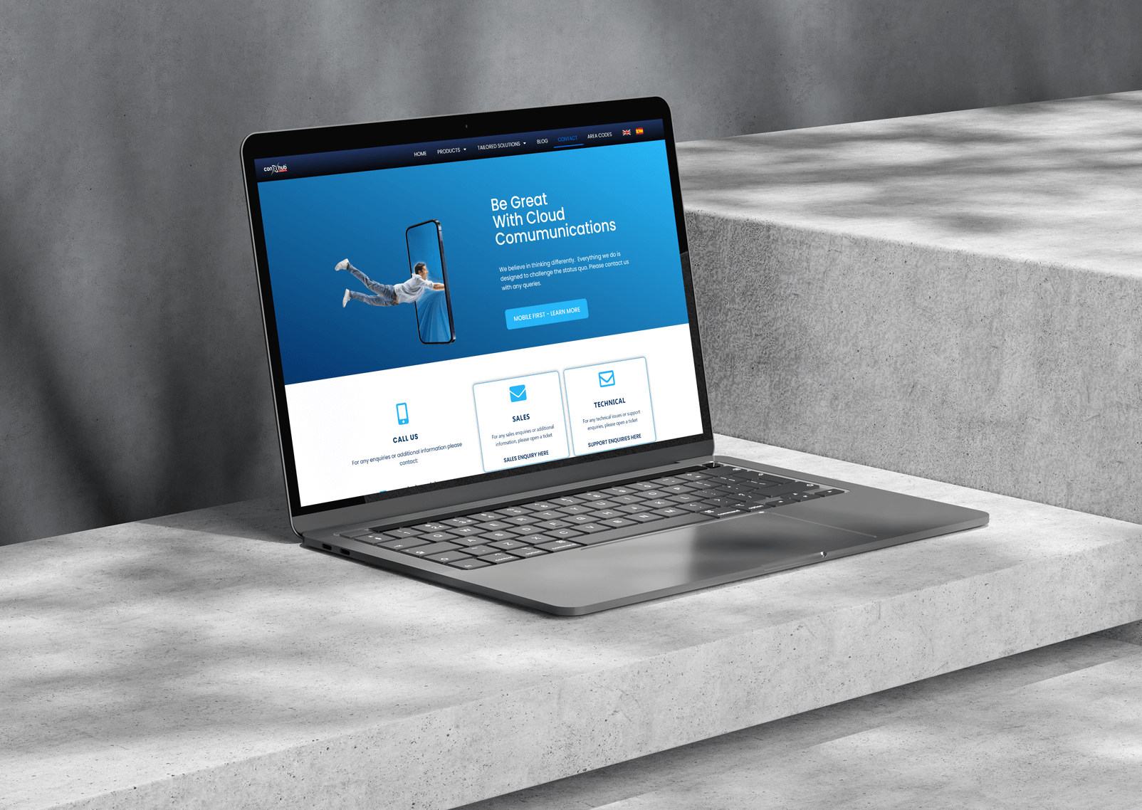 A laptop on a concrete surface displaying a website with the headline "Be Great With Cloud Communications" and an image of a person flying above a smartphone.