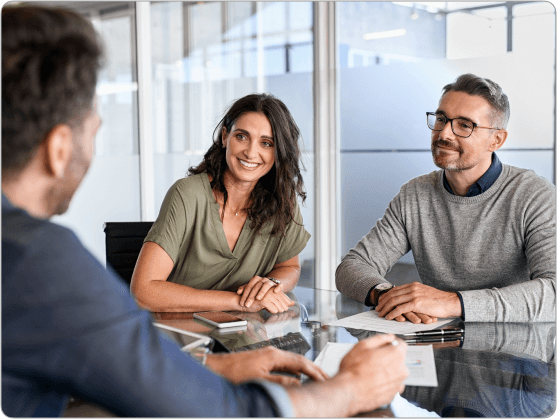 A professional meeting between three individuals in a modern office setting. Two colleagues, a man and a woman, smile attentively at a third person, fostering a collaborative atmosphere.