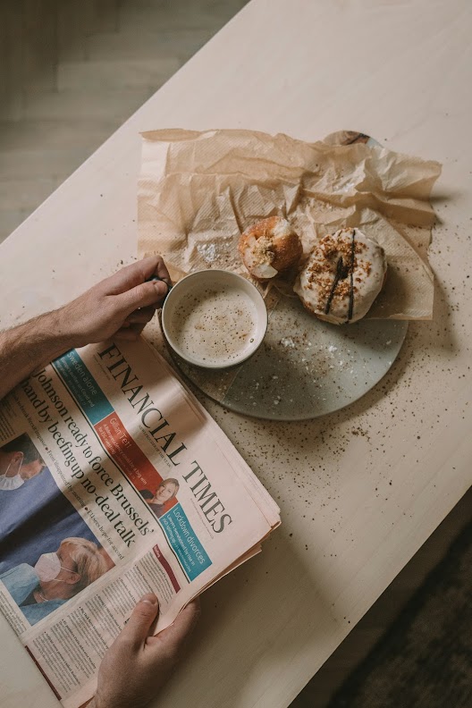 Person reading the Financial Times newspaper while having coffee and donuts for breakfast.