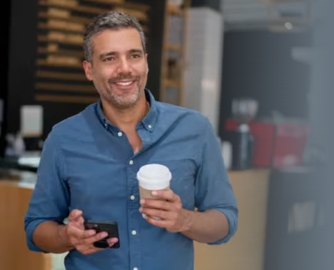 Smiling man holding a coffee cup and smartphone in a casual café setting