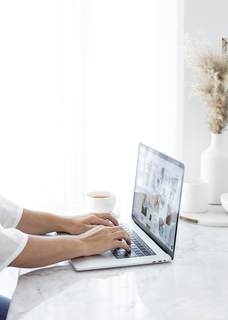 Woman working on laptop, white marble desk, cup of coffee, minimalist workspace